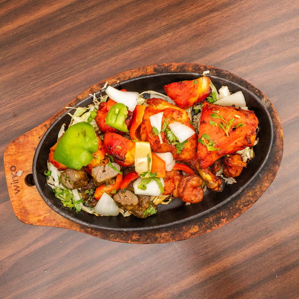 Sizzling platter of tandoori chicken, lamb, shrimp, and vegetables on a wooden table.