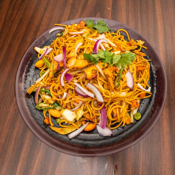 A black plate filled with chicken noodles, red onions, green chilies, and cilantro on a wooden table.