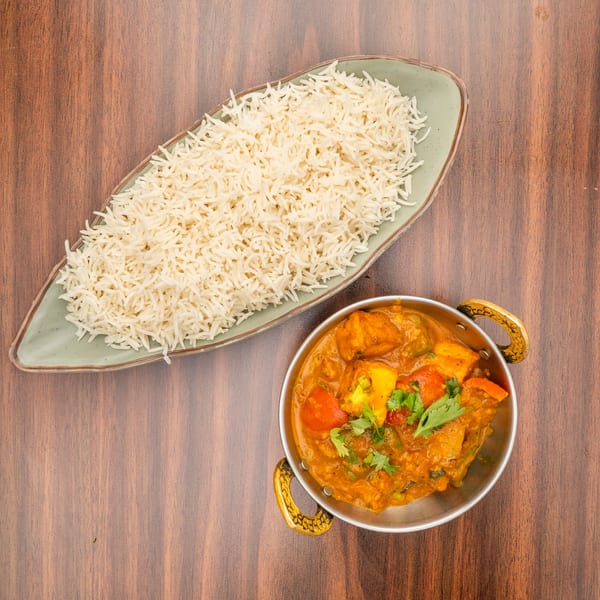 A bowl of paneer curry with bell peppers and cilantro, next to a plate of white rice.