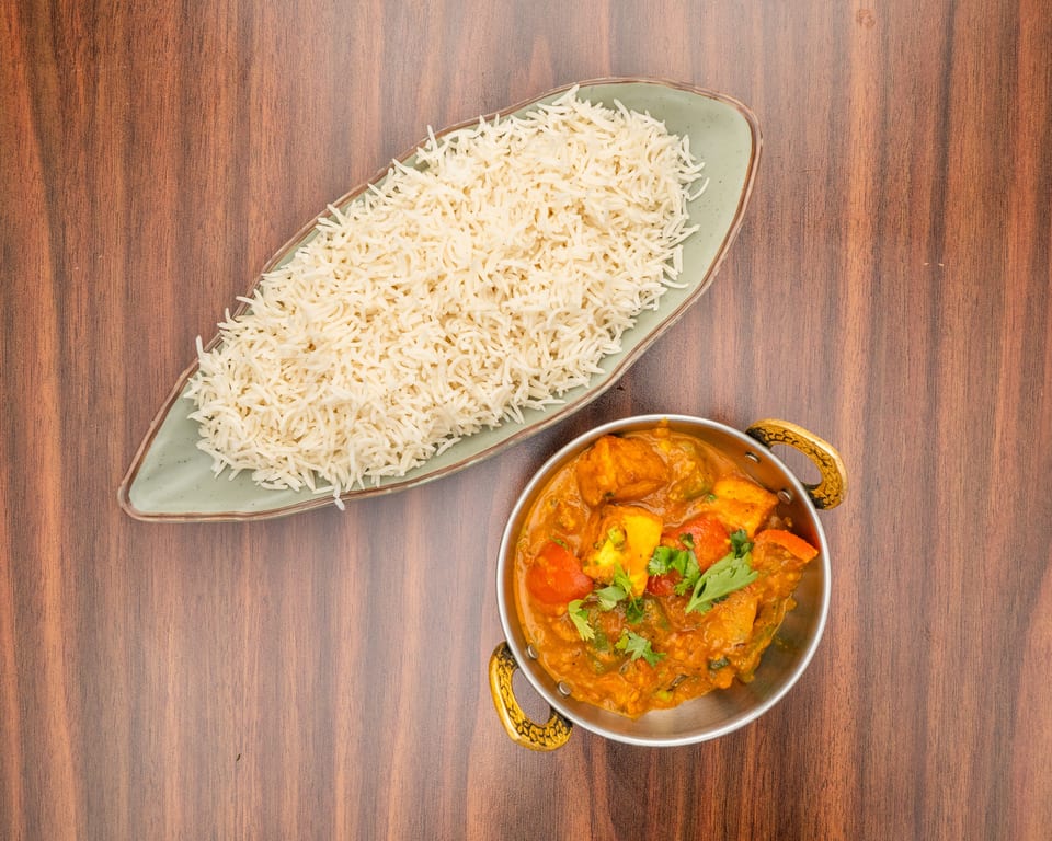 A bowl of paneer curry with bell peppers and cilantro, next to a plate of white rice.