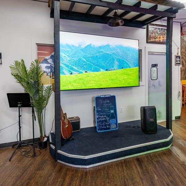 A small stage with a large screen displaying a mountain landscape, a guitar, and a specials board.