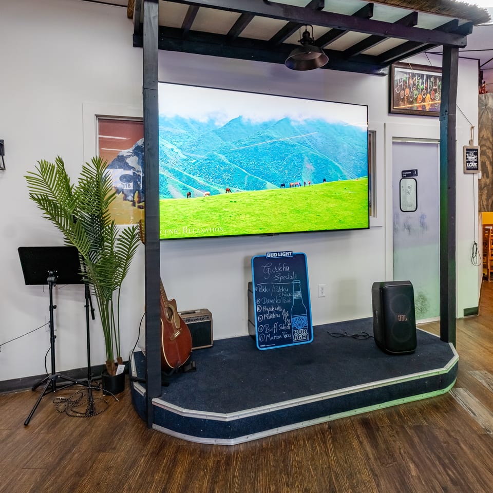 A small stage with a large screen displaying a mountain landscape, a guitar, and a specials board.
