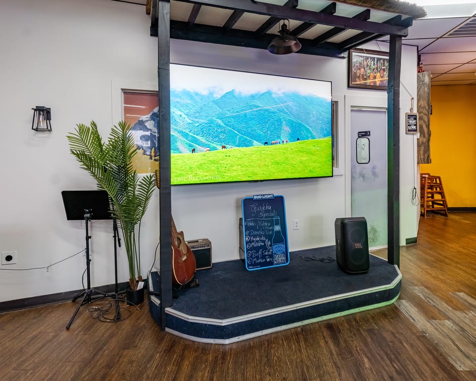A small stage with a large screen displaying a mountain landscape, a guitar, and a specials board.