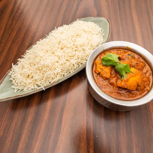 Chicken curry in a metal bowl with cilantro, and a side of white rice on a wooden table.