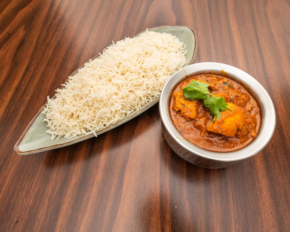 Chicken curry in a metal bowl with cilantro, and a side of white rice on a wooden table.