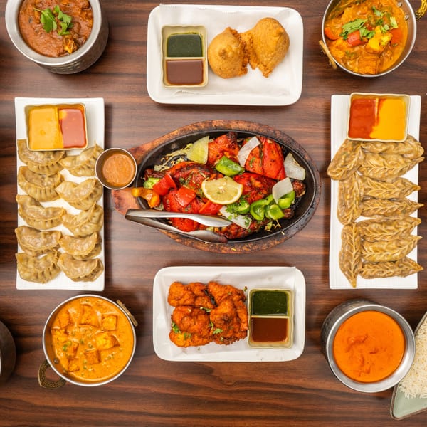 A top-down view of a feast of Indian dishes, including curries, momos, naan, and tandoori chicken.