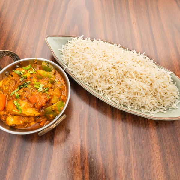 Chicken curry with bell peppers and cilantro in a metal bowl, served with a side of white rice.