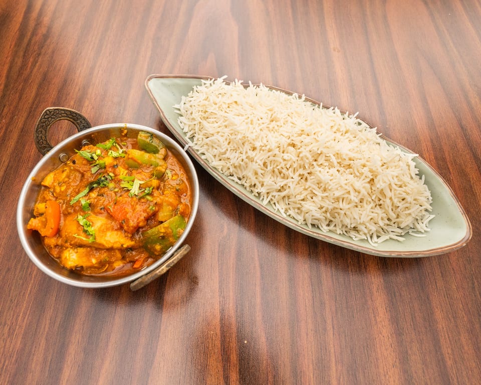 Chicken curry with bell peppers and cilantro in a metal bowl, served with a side of white rice.