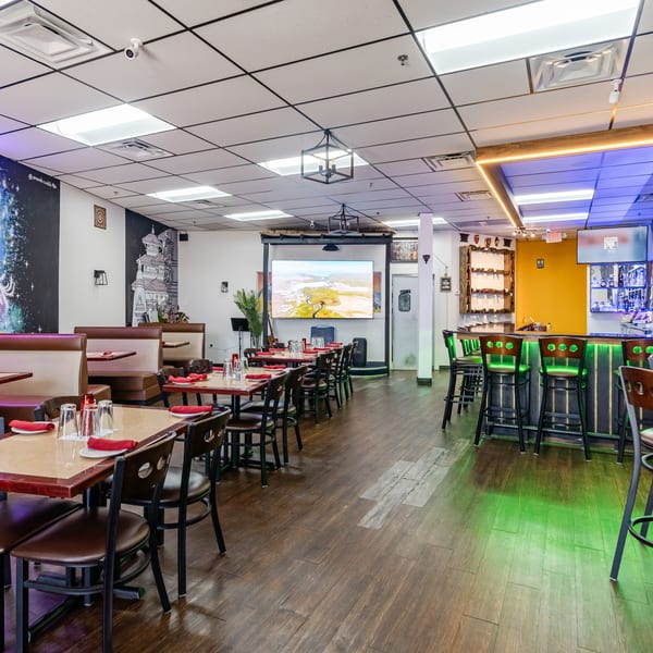 Spacious restaurant interior with dining tables, booths, a bar with green lighting, and vibrant wall murals.