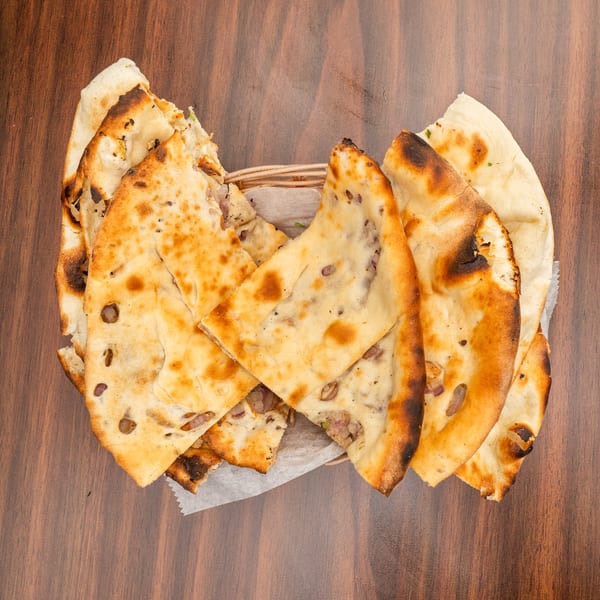 A basket of freshly baked naan bread with visible char marks and red onion pieces.