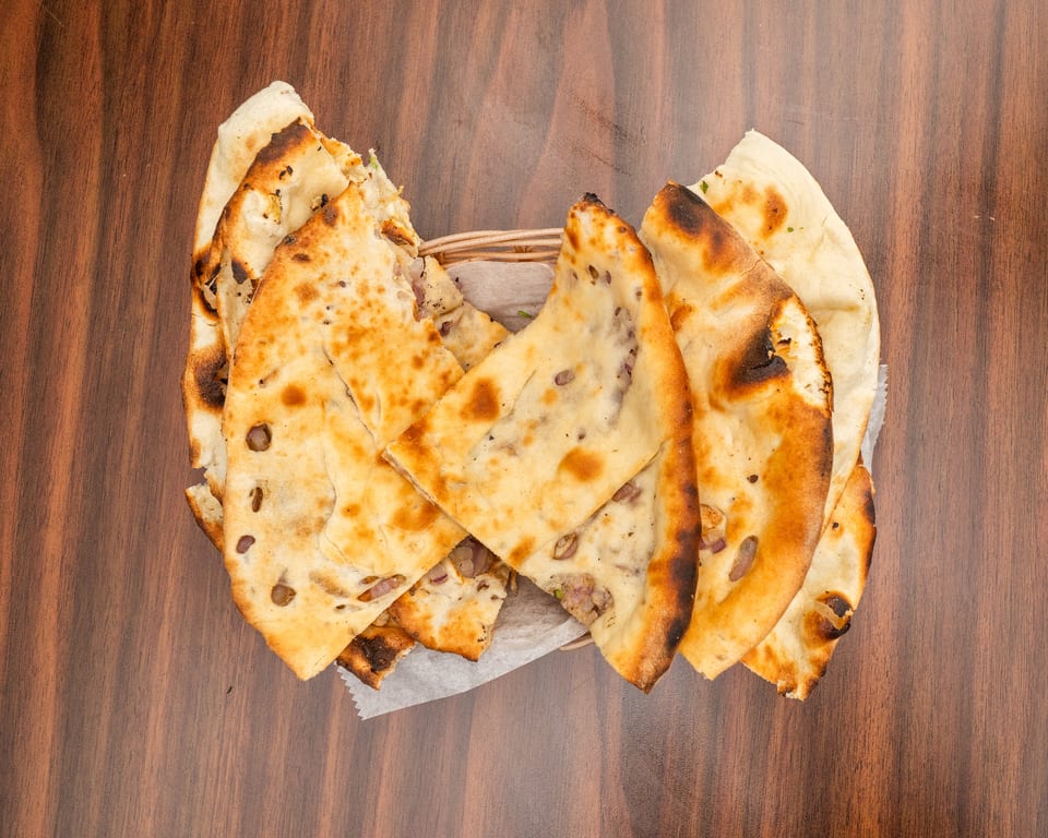 A basket of freshly baked naan bread with visible char marks and red onion pieces.