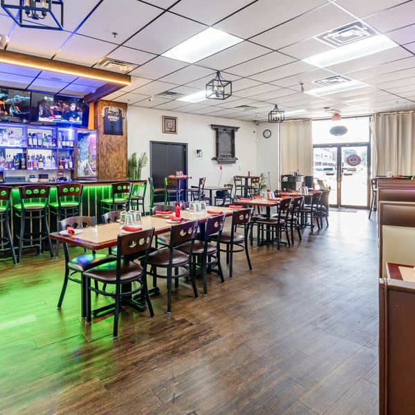 Restaurant interior with a glowing green bar, dining tables with red napkins, and booth seating.