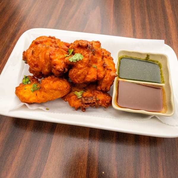 Crispy fried pakora, garnished with cilantro, served with green and brown dipping sauces.