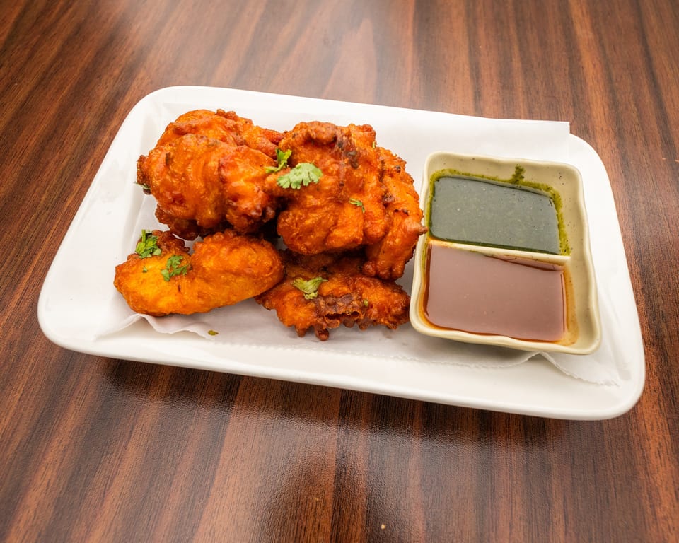 Crispy fried pakora, garnished with cilantro, served with green and brown dipping sauces.