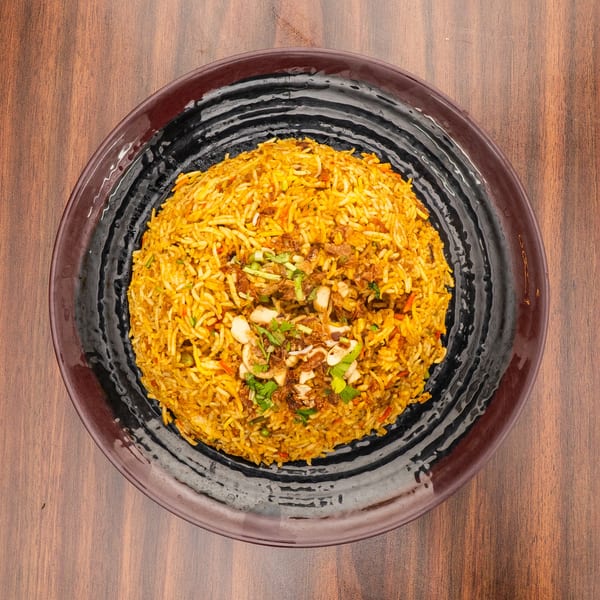 A large serving of yellow biryani rice with cashews, fried onions, and herbs on a black plate.