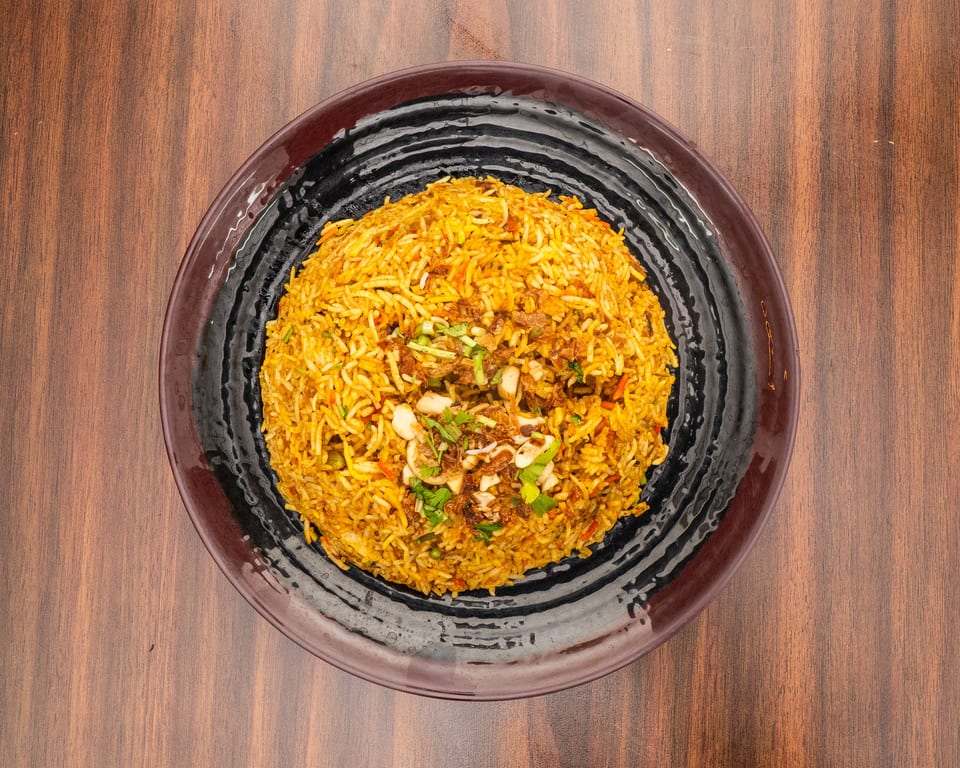A large serving of yellow biryani rice with cashews, fried onions, and herbs on a black plate.