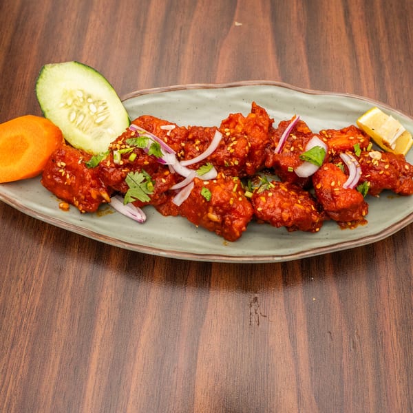 Spicy red chicken wings with sesame seeds, cilantro, and red onions, served with cucumber, carrot, and lemon.
