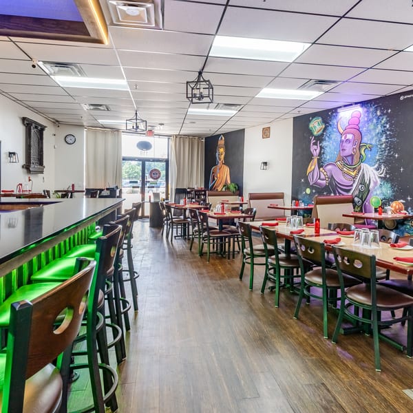 Restaurant interior with a long bar and green stools, dining tables, and colorful murals on the walls.