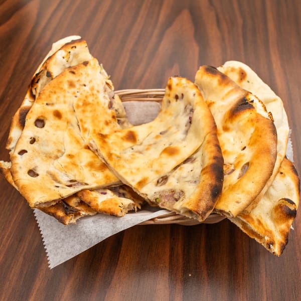 A basket of freshly baked naan bread, some pieces folded, on a dark wooden table.