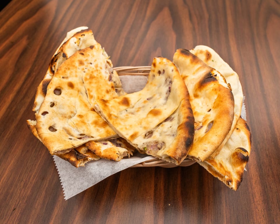 A basket of freshly baked naan bread, some pieces folded, on a dark wooden table.