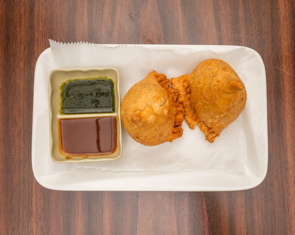Two golden-brown samosas and a divided dish of green and brown chutneys on a white plate.