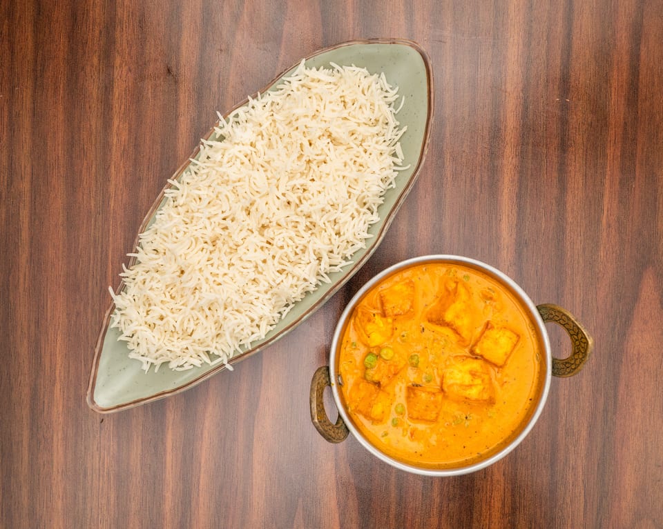 Overhead view of paneer butter masala with peas in a metal bowl and basmati rice on a green plate.